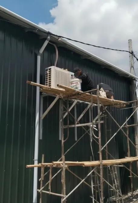 Teknisi memasang unit AC outdoor di atas scaffolding